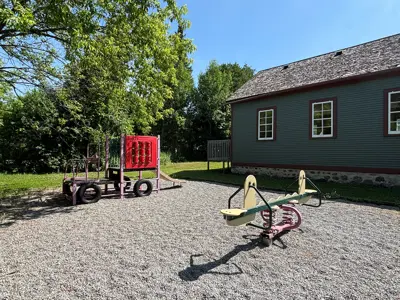 small playground with seesaw and climbing structure with schoolhouse in background