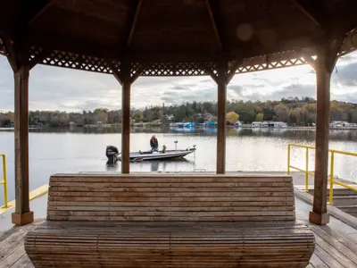 Inside of Gazebo with focus on wooden bench and people on fishing boat in background