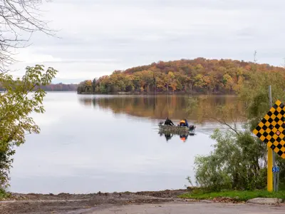 dead end road with water access area with people on fishing boat and island visible in background