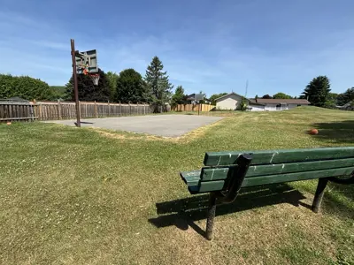 Old Camborne Schoolhouse Playground focused on a basketball court from the perspective of a nearby bench