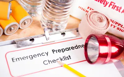 clipboard with paper that reads "emergency preparedness checklist" surrounded by various emergency tools such as water, first aid kit, flashlight, and batteries
