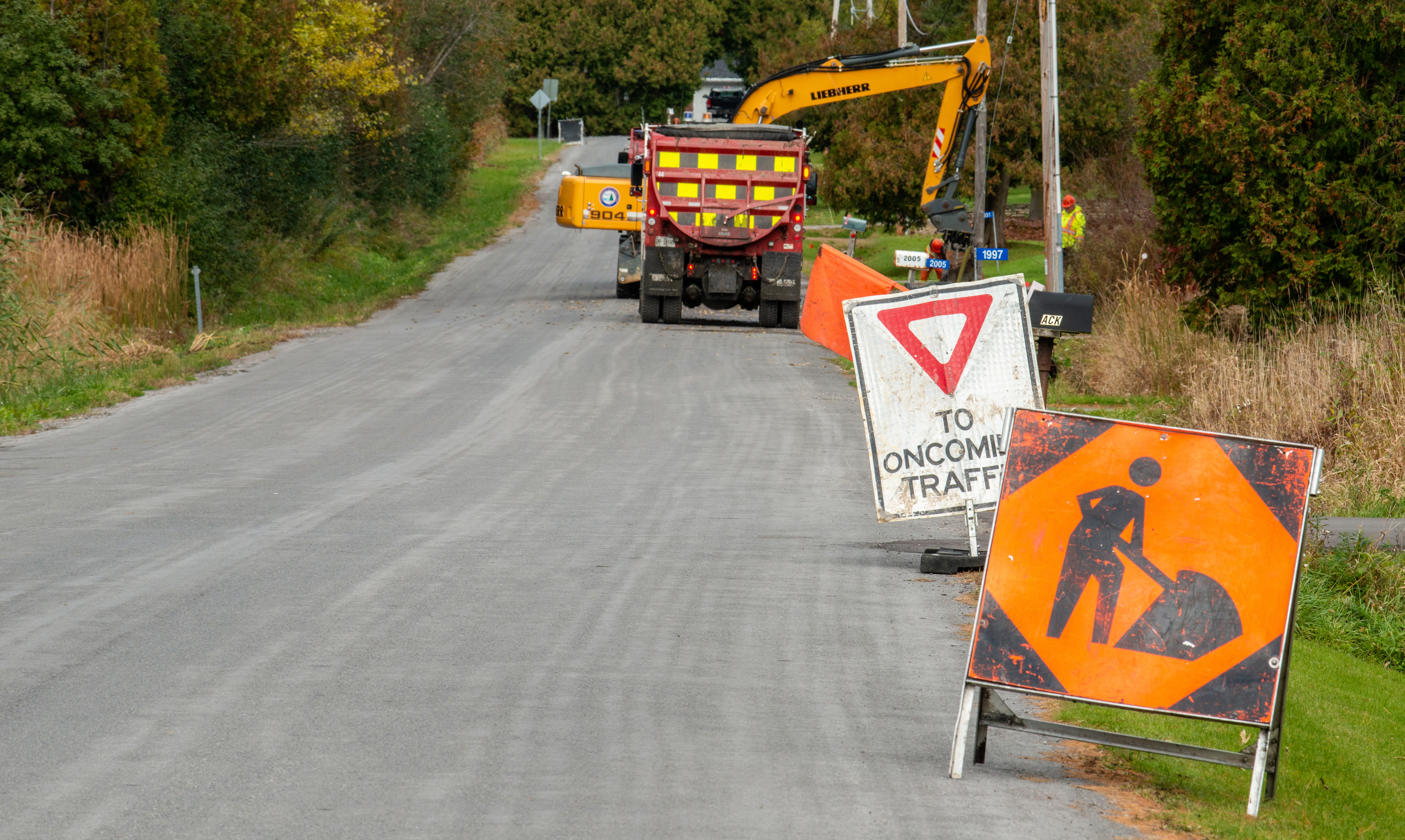 signs indicating road closure with a dump truck and excavator at work in the background