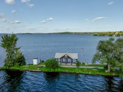 Drone view of a pavillion with a sign reading "Harwood", situated on a small strip of land that is surrounded by Rice Lake