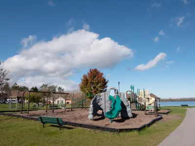Optimist Park focused on a large climbing structure, swings, and benches surrounded by greenery