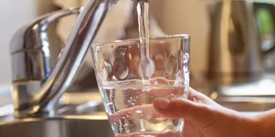 hand filling up glass of water from sink