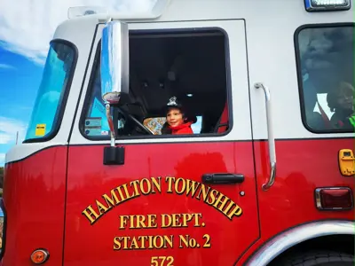 child dressed up as fire fighter sits in driver's seat of fire truck