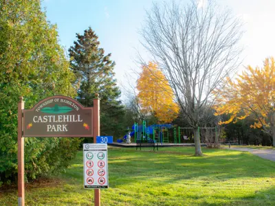 Castlehill Park sign featuring relevant by-laws, the playground climbing structures and swings are visible in the background