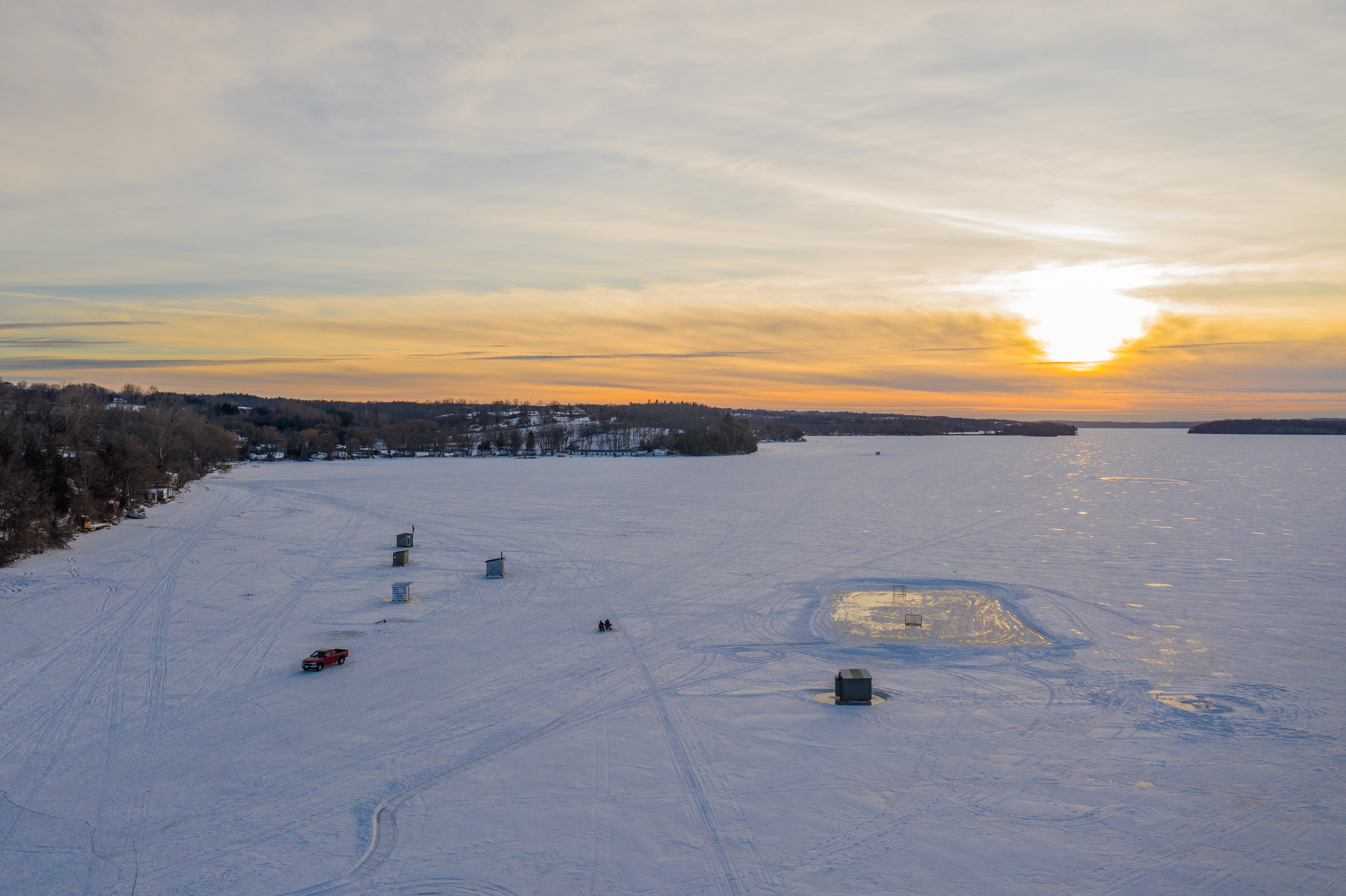 Drone view of a sunset over frozen Rice Lake with a few small ice fishing cabins set up