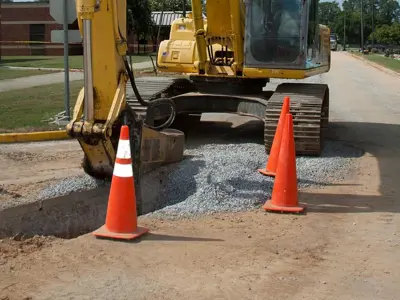 excavator with arm down next to a pit surrounded by pylons