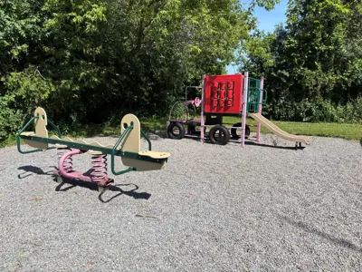 small playground with seesaw and climbing structure with schoolhouse in background