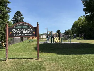 sign reading "Old Camborne Schoolhouse Playground" with playground and basketball court in background